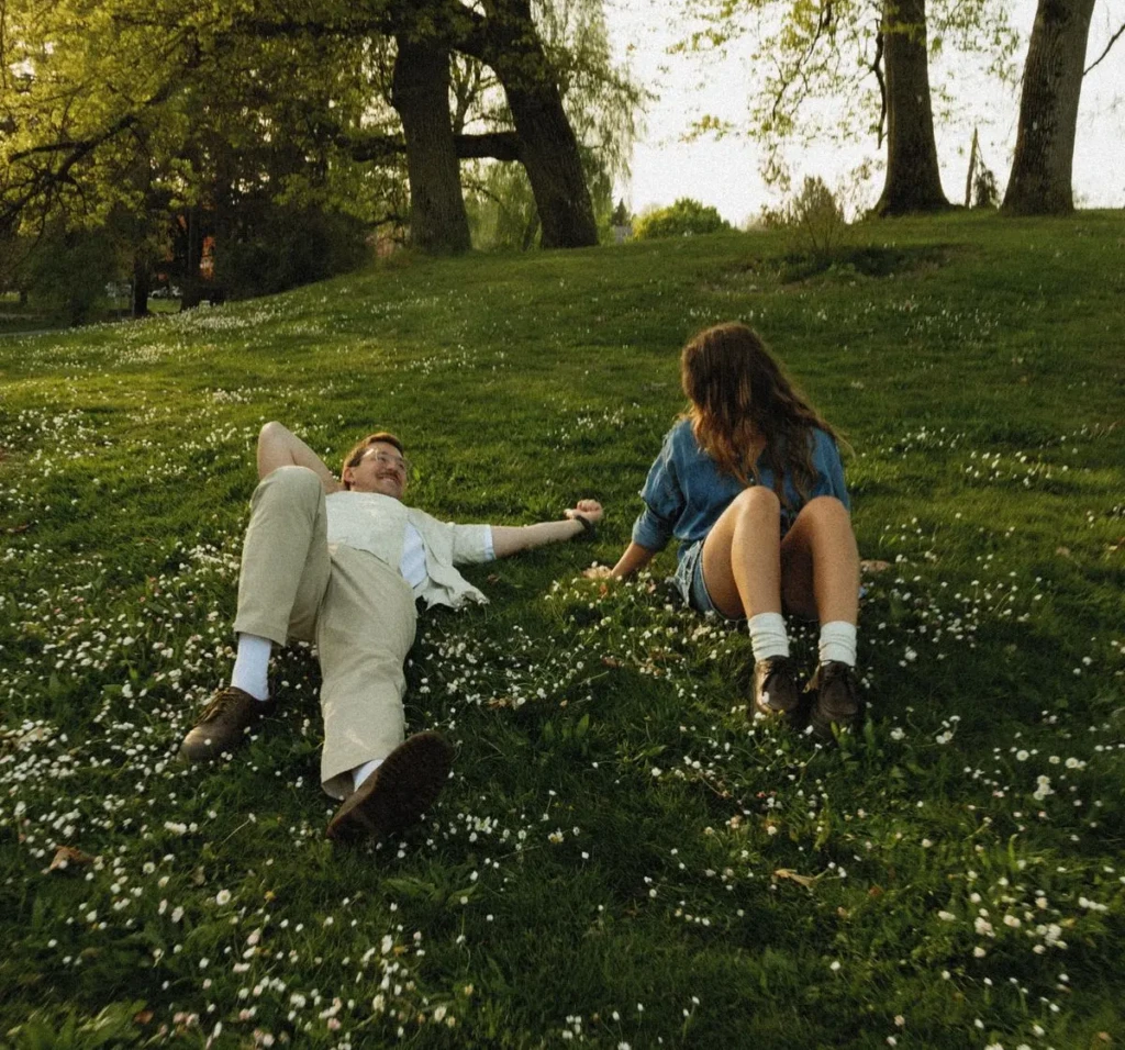 دختر و پسر روی چمن، دختر نشسته و پسر خوابیده، هر دو با لبخند به هم نگاه میکنند