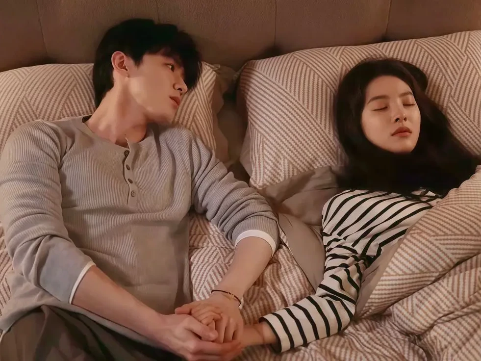 زوج عاشق در رختخواب، مرد دست زن را گرفته و در فکر فرو رفته، زن در خواب آرام شبانه